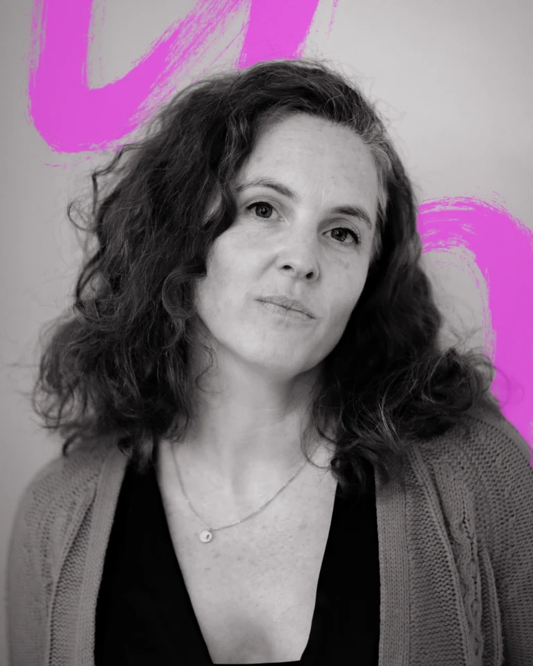 A close up black and white portrait of a woman with long dark curly hair. Behind her is a hand-drawn scribble in neon pink.