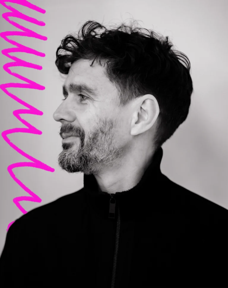 a close up black and white portrait of a man with short dark curly hair looking off to the left. Next to him is a hand-drawn neon pink scribble.