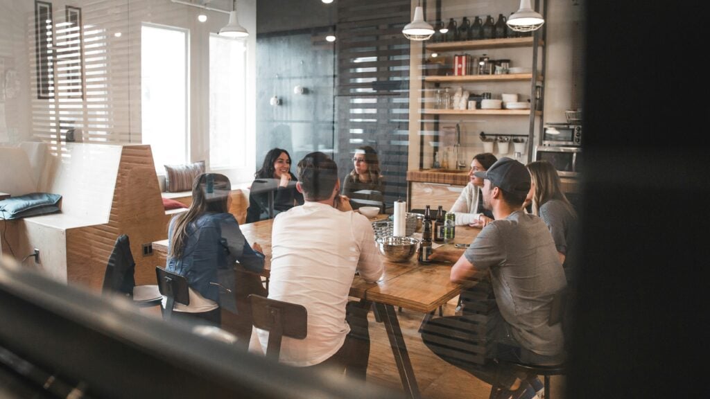 A team of people sat around a large wooden table, in a clean, modern looking co-working space.