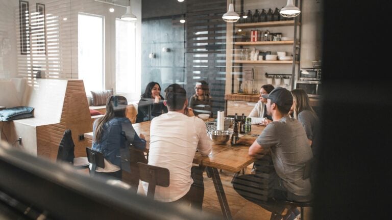 A team of people sat around a large wooden table, in a clean, modern looking co-working space.